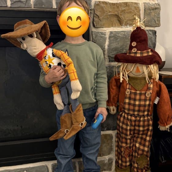 Brad's son holding a cowboy doll next to a scarecrow, his face covered with a smiley emoji
