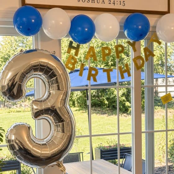 A silver number 3 balloon in front of a Happy Birthday banner and blue and white balloons