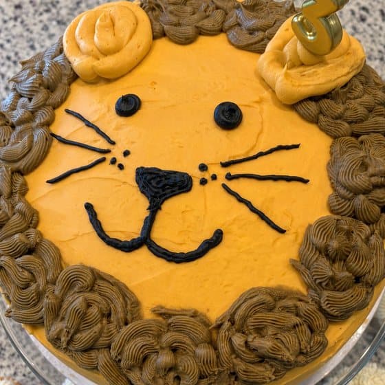 A lion face cake with orange frosting and a swirled brown frosting mane